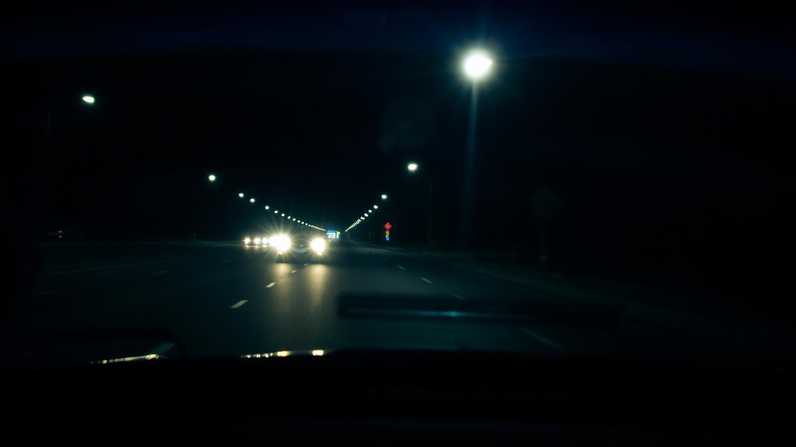 Visão do interior de um carro à noite com faróis e reflexos
